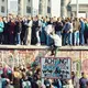 Menschen auf und vor der Berliner Mauer vor dem Brandenburger Tor am Tag des Mauerfalls am 9. November 1989. Im Vordergrund das Warnschild mit der Aufschrift „Achtung, Sie verlassen jetzt Westberlin“.