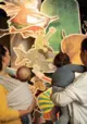 Eltern mit Kleinkindern stehen vor bunten Illustrationen aus Preußlers Büchern.